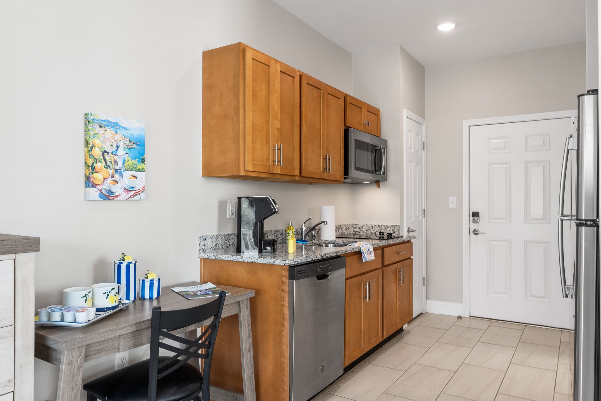 A compact kitchen with wooden cabinets, a stainless steel refrigerator, a microwave, and a coffee maker.