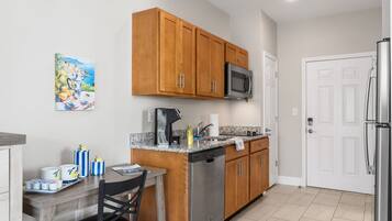 A compact kitchen with wooden cabinets, a stainless steel refrigerator, a microwave, and a coffee maker.