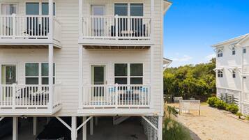 A multi-story building with balconies, a covered parking area, and a sandy ground.