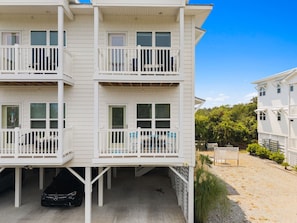 A multi-story building with balconies, a covered parking area, and a sandy ground.