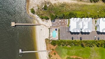 An aerial view of a coastal property with a swimming pool, parking area, and a dock.