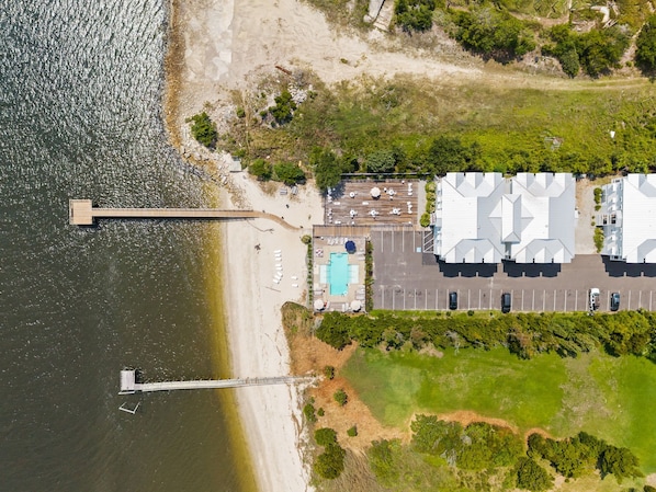 An aerial view of a coastal property with a swimming pool, parking area, and a dock.