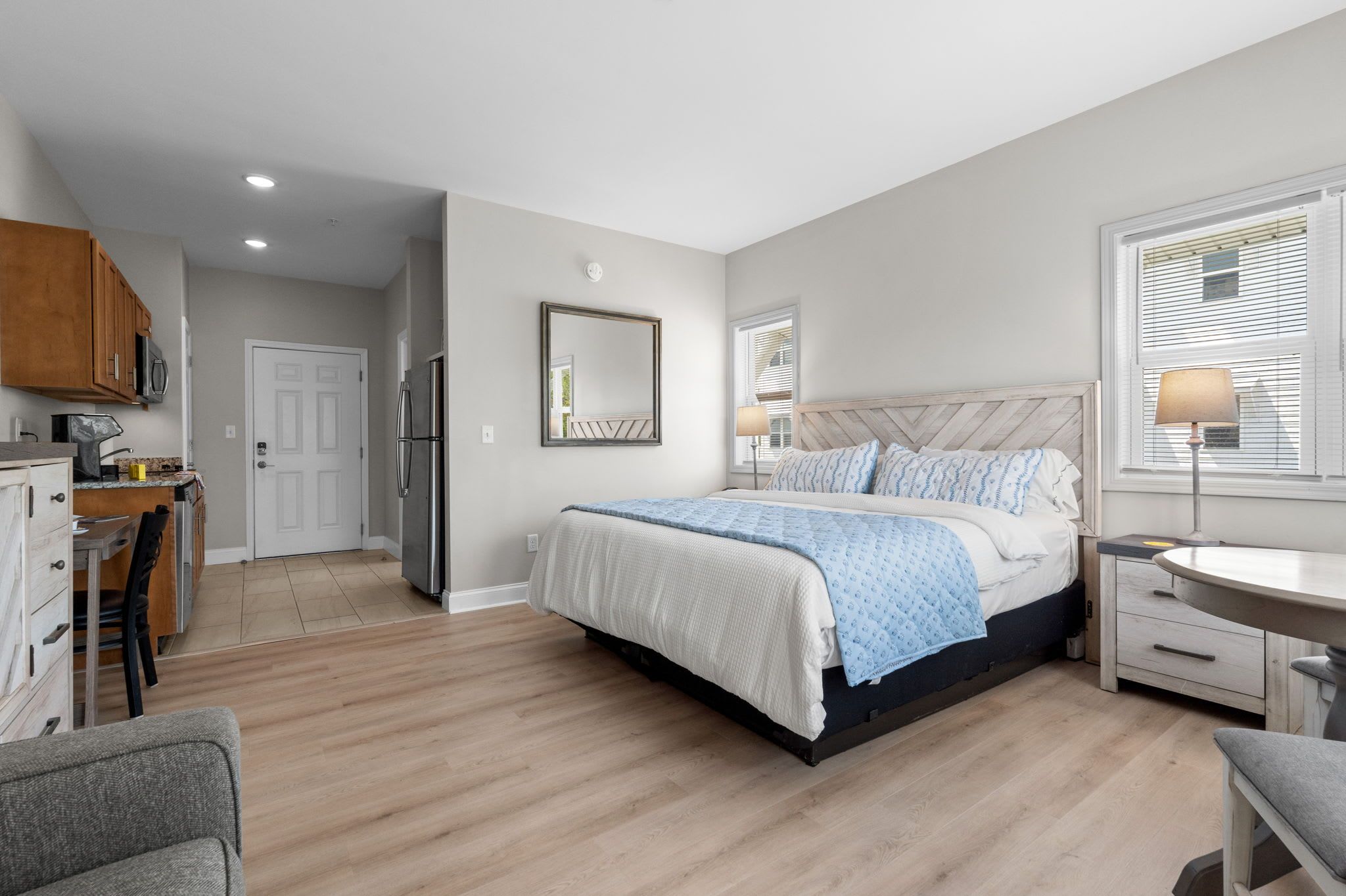 A bedroom with a bed, bedside tables, a window, and a kitchen area with cabinets and appliances.