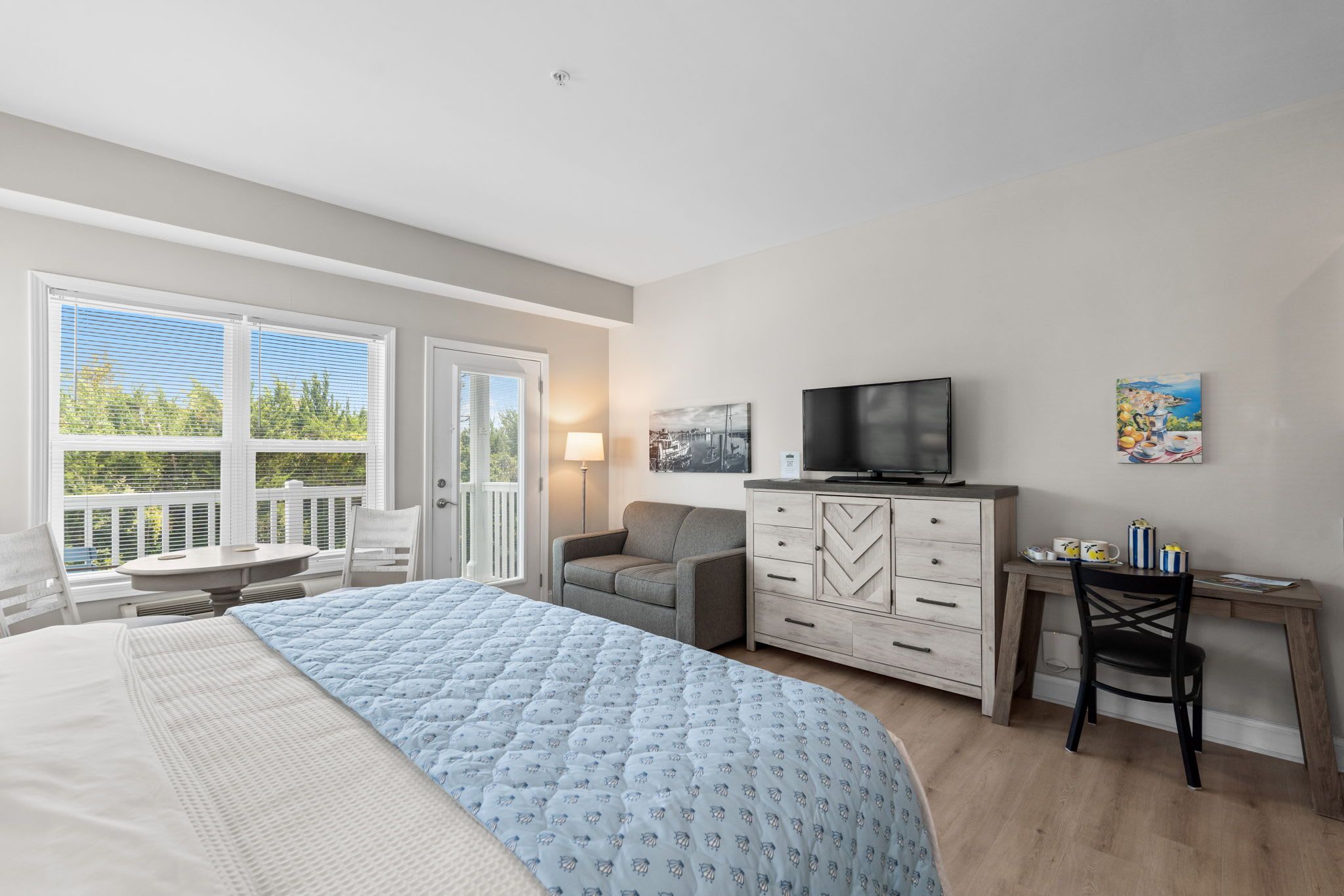 A bedroom with a bed, a desk, a chair, a television, and a painting on the wall.