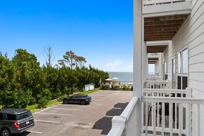 Un espace de stationnement avec une voiture, une vue sur la mer et un bâtiment doté d’un balcon.