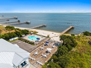 Une propriété située en bord de mer, dotée d’une piscine, de chaises longues et d’une jetée qui s’avance dans l’eau.