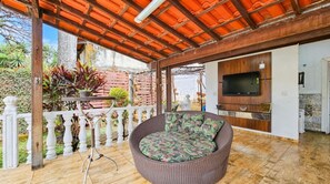 A covered outdoor seating area with a wicker sofa and a TV mounted on a wooden wall. - Casa com Piscina e Sauna no Granja Vista Alegre (Contagem)