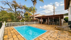 A swimming pool with a tiled deck, surrounded by a white fence, and a covered outdoor seating area with chairs. - Casa com Piscina e Sauna no Granja Vista Alegre (Contagem)