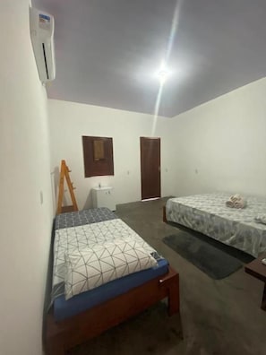 A bedroom with two beds, a wooden bench, a desk, and an air conditioning unit. - Pousada do Beto (Barreirinhas)