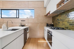 A modern kitchen with white cabinetry, a stainless steel sink, a built-in oven, and a gas stove. - The Cove Escape - Cooks Beach Holiday Home (Cooks Beach)