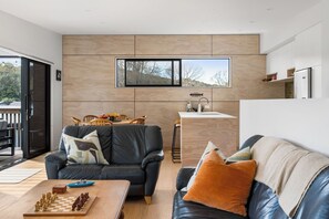 A modern living space with a dining area, a kitchen, and a view of the outdoors. - The Cove Escape - Cooks Beach Holiday Home (Cooks Beach)