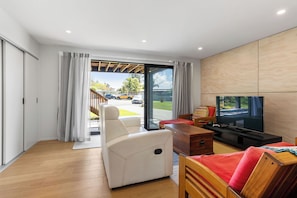 A modern living room with a sofa, a TV, and a wooden coffee table. - The Cove Escape - Cooks Beach Holiday Home (Cooks Beach)