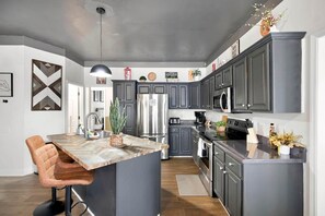 Une cuisine moderne avec des meubles de couleur sombre, des appareils en acier inoxydable et un îlot central doté de sièges.