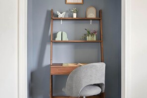 Un bureau en bois avec une chaise grise, une étagère ornée d’objets décoratifs et un panneau fixé au mur.