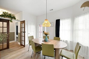 Un coin repas comprenant une table ronde, des chaises, un luminaire suspendu et une porte à motifs géométriques.