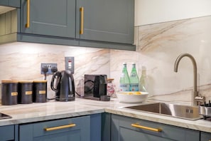 A kitchen with a marble countertop, a coffee maker, a kettle, a toaster, and two bottles of water. - HR2 - Charming 1-Bed near Holland Park (London)