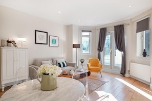 A modern living room with a sofa, armchair, and a dining table with a vase of flowers. - HR2 - Charming 1-Bed near Holland Park (London)