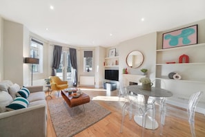 A modern living room with a sofa, a coffee table, and a dining area with chairs and a table. - HR2 - Charming 1-Bed near Holland Park (London)