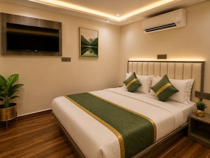 A hotel room with a large bed, a flat-screen TV mounted on the wall, an air conditioning unit, and a painting of a mountain landscape. - The Crown Hotel Lokhandwala Andheri  (Mumbai)