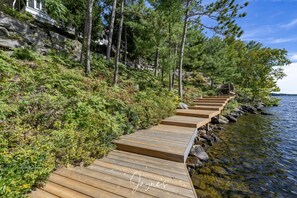 Une promenade en bois longeant une côte rocheuse, bordée d’une végétation luxuriante et d’arbres.