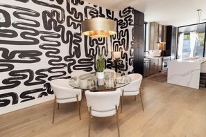 A modern kitchen with a dining area, featuring a round glass table with chairs, a pendant light, and a patterned wall. - Luxury SoCo Haven w/ 6Sleep, Hot Tub & Gym (Austin)