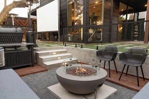 An outdoor patio with a fire pit, seating, and a view of a modern building. - Luxury SoCo Haven w/ 6Sleep, Hot Tub & Gym (Austin)
