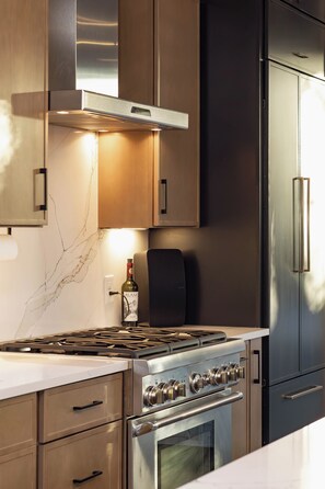 A modern kitchen with stainless steel appliances, wooden cabinets, and a wine bottle on the counter. - Luxury SoCo Haven w/ 6Sleep, Hot Tub & Gym (Austin)