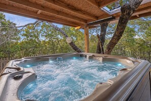 A hot tub with a wooden structure overhead, surrounded by trees.