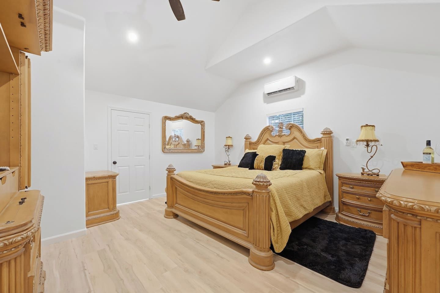 A bedroom with a wooden bed, bedside tables, a mirror, and an air conditioning unit.