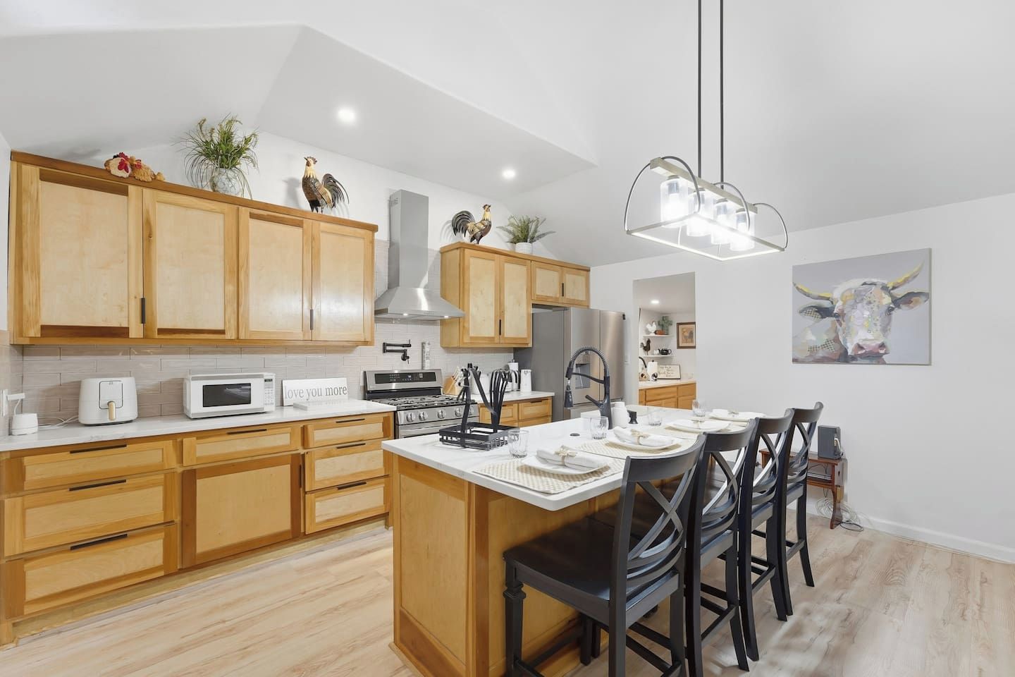 A modern kitchen with wooden cabinets, a central island, and a dining area with chairs.