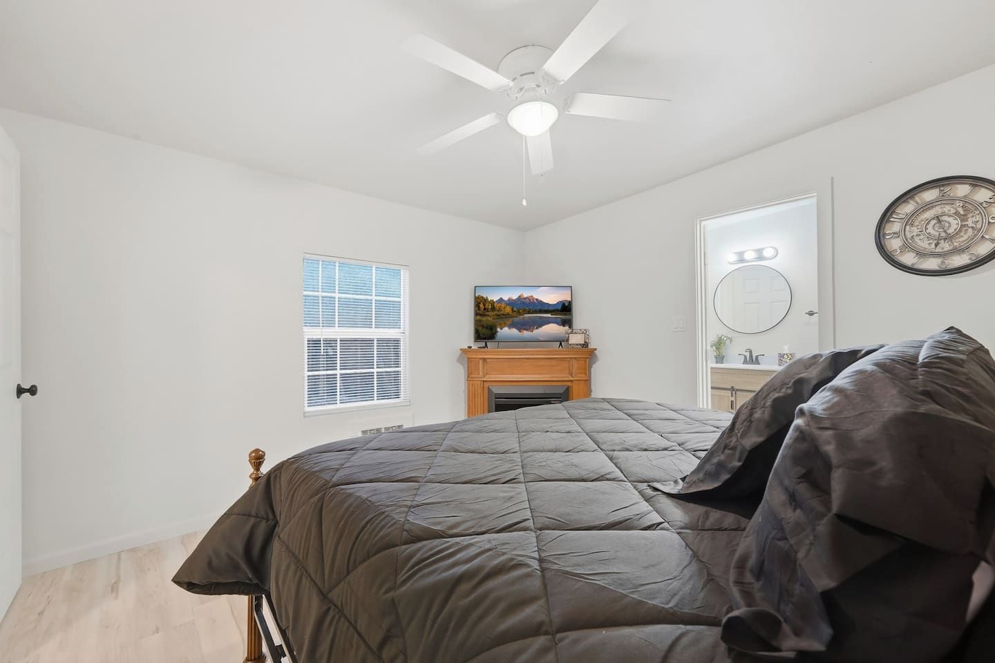 A bedroom with a bed, a ceiling fan, a fireplace, a window, and a wall clock.