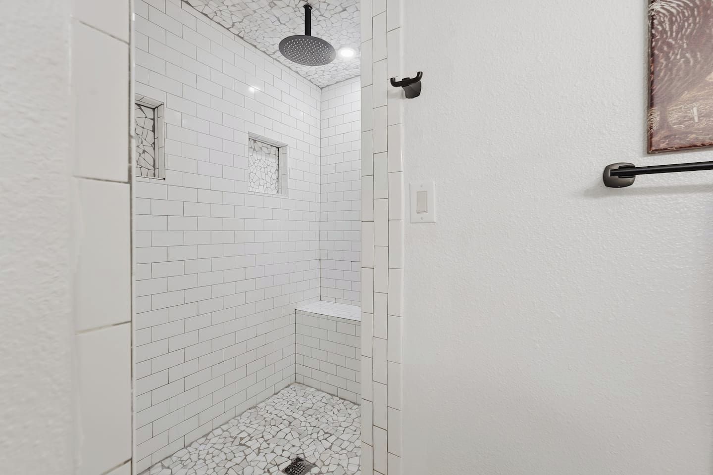 A bathroom with white tiled walls and floor, a shower with a black showerhead, and a towel rack on the wall.