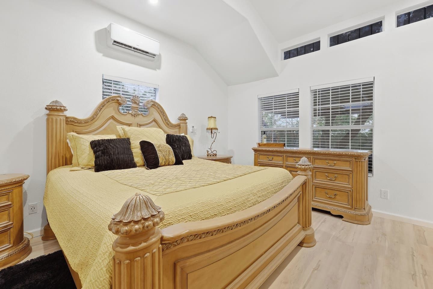 A bedroom with a large bed, a dresser, a nightstand, and a window with blinds.