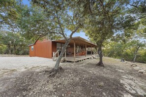 Un chalet rustique doté d’un porche, entouré d’arbres et d’un sol en gravier.