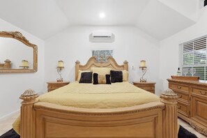 Ein Schlafzimmer mit einem großen Bett, zwei Nachttischen, einem Spiegel, einer Klimaanlage und einem Fenster mit Jalousien.