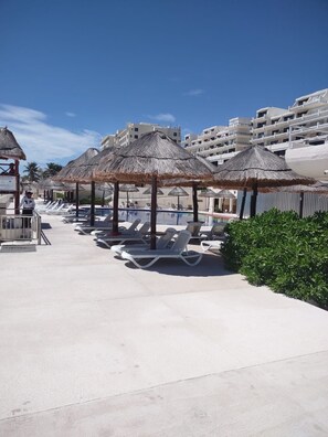 Ein Poolbereich eines Resorts mit Liegestühlen und Reetdachschirmen, umgeben von Gebäuden.
