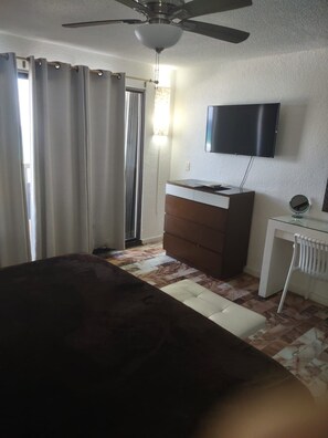 Ein Schlafzimmer mit Bett, Kommode, Schreibtisch, Fernseher und Deckenventilator.