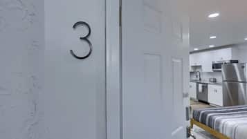 A modern bedroom with a bed, a door with the number 3, and a view into a kitchen area with appliances.