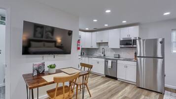 A modern kitchen with white cabinets, stainless steel appliances, and a dining area with a wooden table and chairs.