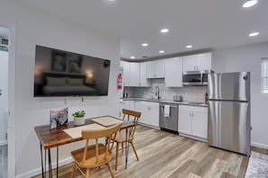 Une cuisine moderne avec des meubles blancs, des appareils en acier inoxydable et un coin repas comprenant une table et des chaises en bois.
