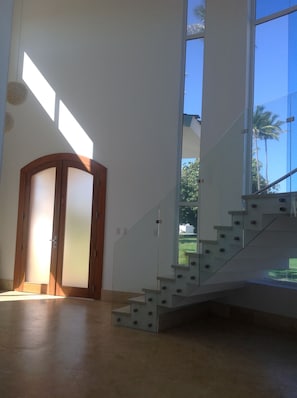 A modern interior with a staircase leading to a balcony, large windows, and a wooden door. - Paradise in Puerto Plata! Spacious villa with private pool and much more!!!! (Santo Domingo Este)