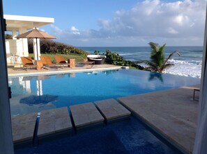 Une piscine avec vue sur l’océan, des chaises longues et un espace salon abrité.