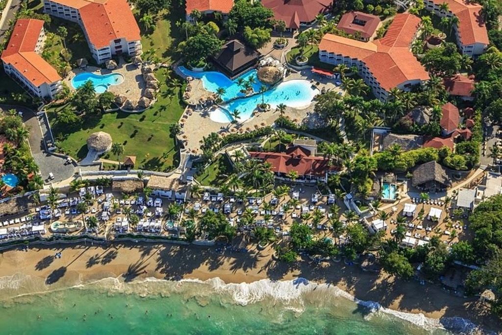 Eine Vogelperspektive zeigt ein Resort mit mehreren Schwimmbecken, Strandvillen und einem Strand.