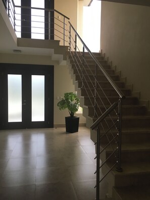 Eine Treppe mit Metallgeländer führt zu einer oberen Etage, ein Blumentopf und eine Tür mit satinierten Glasscheiben.