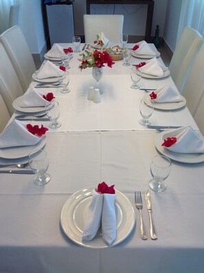 Ein formell gedeckter Esstisch mit weißer Tischdecke, Besteck und roten Blumenarrangements in der Mitte.