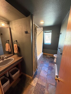 A bathroom with a sink, mirror, towel rack, shower curtain, and a window providing natural light. - Mountain top A-frame with hot tub and Sauna (Fairplay)