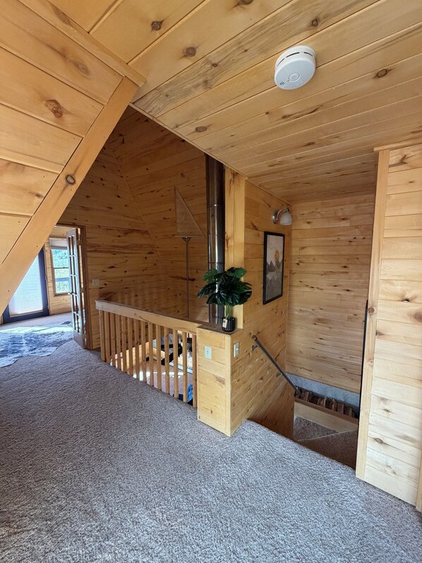 A wooden interior with a staircase, a ceiling vent, and a potted plant.