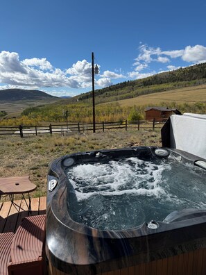 A hot tub on a wooden deck with a view of a mountainous landscape.
