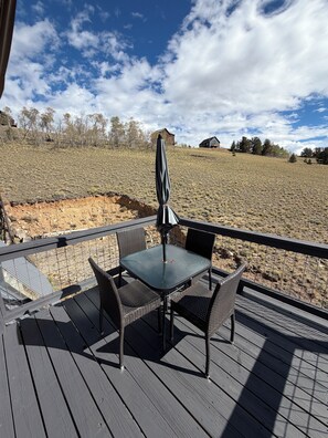 A deck with a table and chairs, overlooking a dry landscape with sparse vegetation and distant buildings. - Mountain top A-frame with hot tub and Sauna (Fairplay)