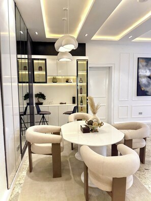 A modern dining area with a round table, cushioned chairs, and pendant lighting. - Smart Luxury 2BR | Starlink • PS5 • 24/7 Power • Modern Living (Abuja)